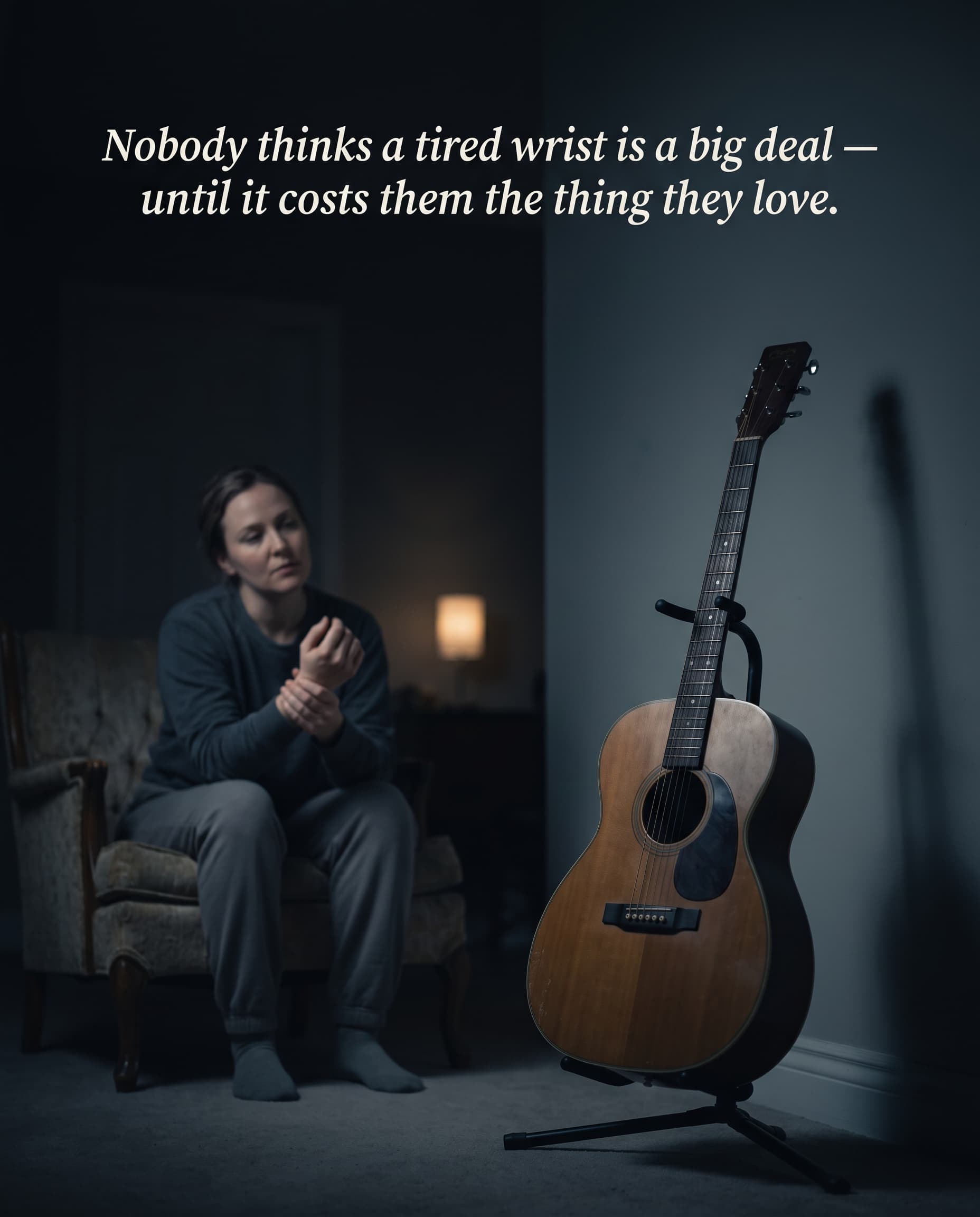 A person sitting in a dim room quietly rubbing an aching wrist while a guitar sits untouched on a stand nearby.